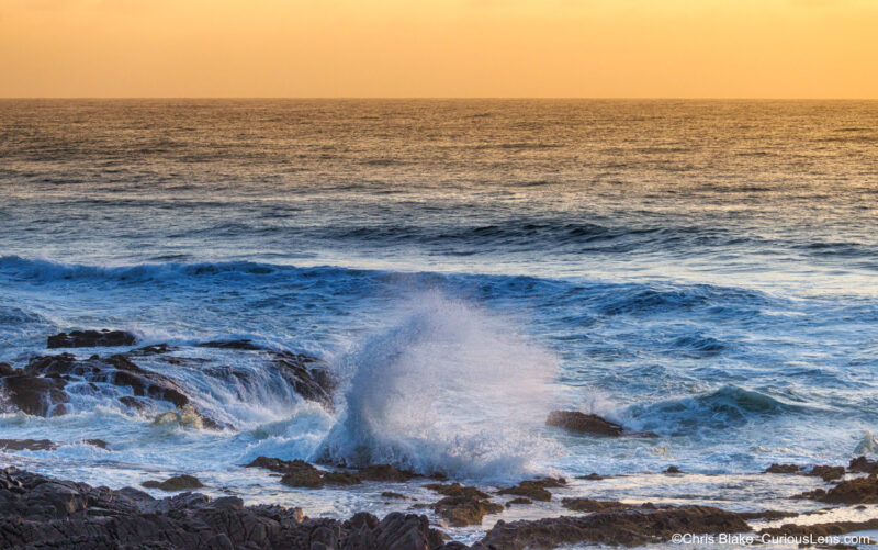 Thor’s Well at Cape Perpetua during sunset, with ocean waves exploding over lava rock beneath a golden sky on the Oregon Coast.