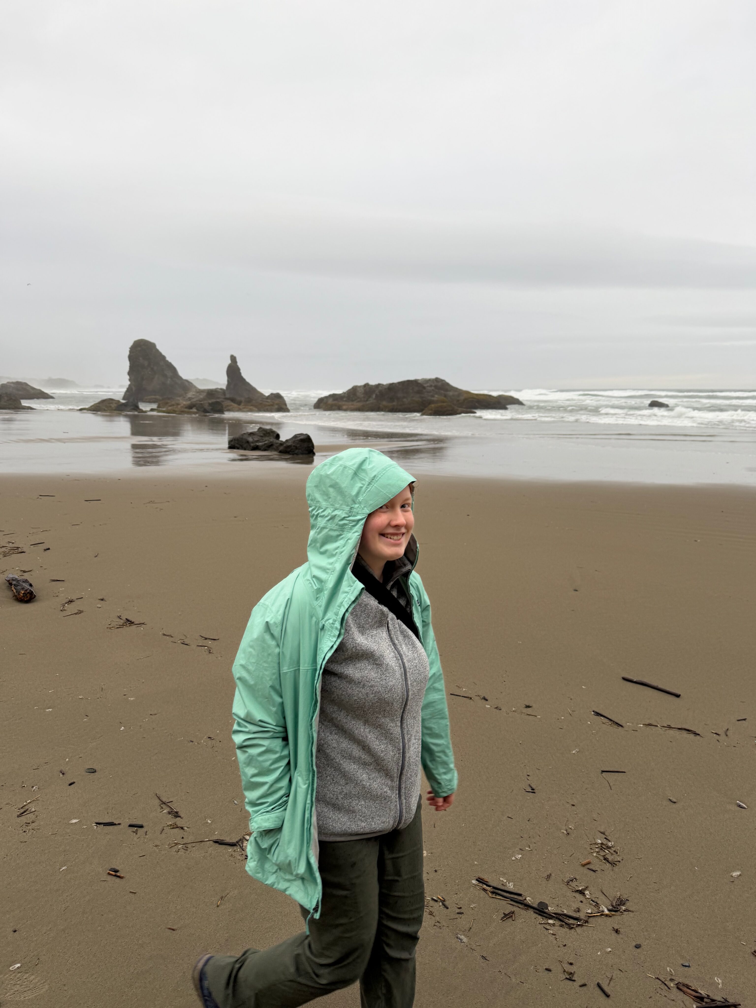 Cami walking on Bandon Beach in the rain with sea stacks in the distance.