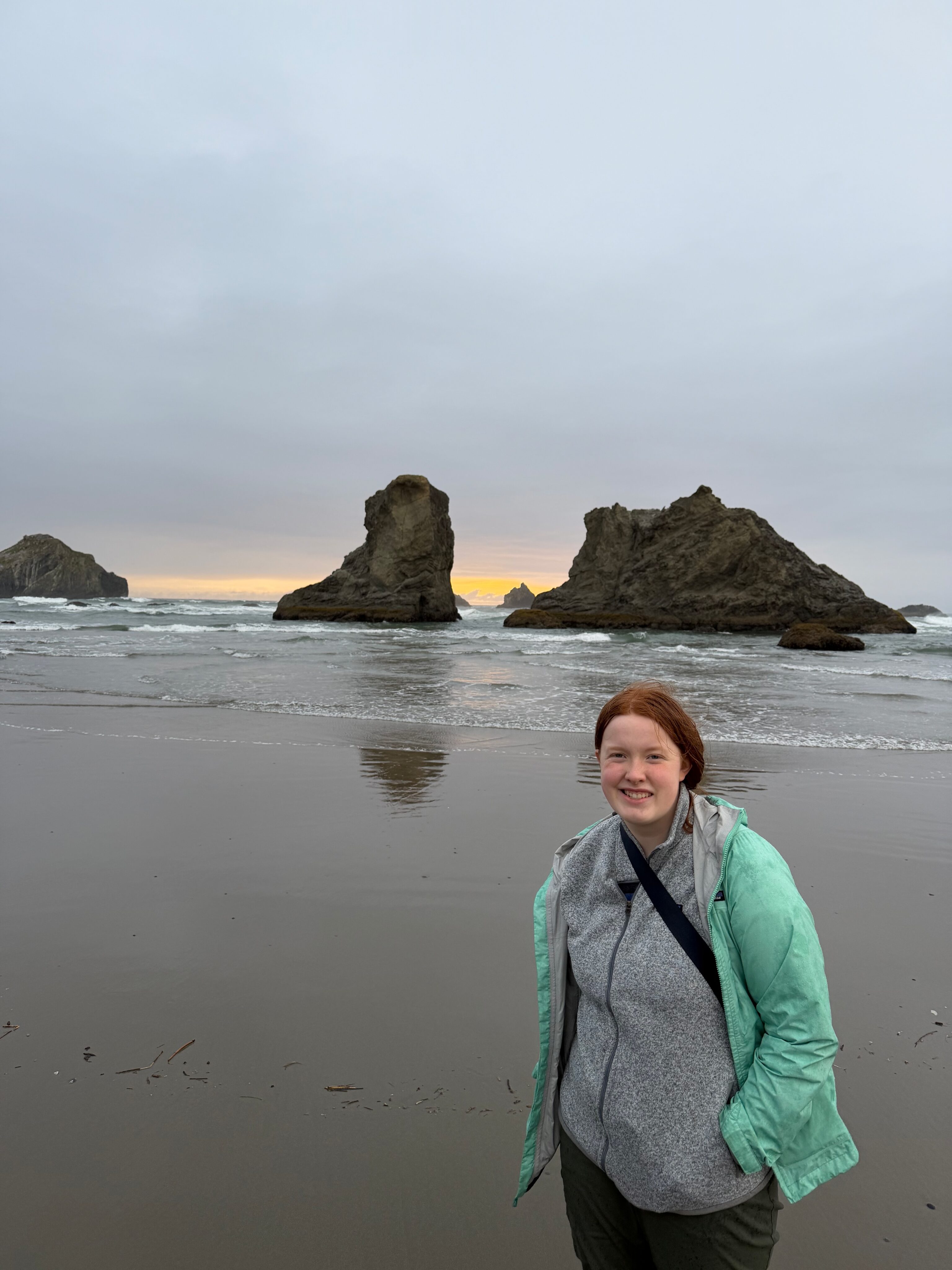 Cami standing on Bandon Beach near sunset with sea stacks behind her.