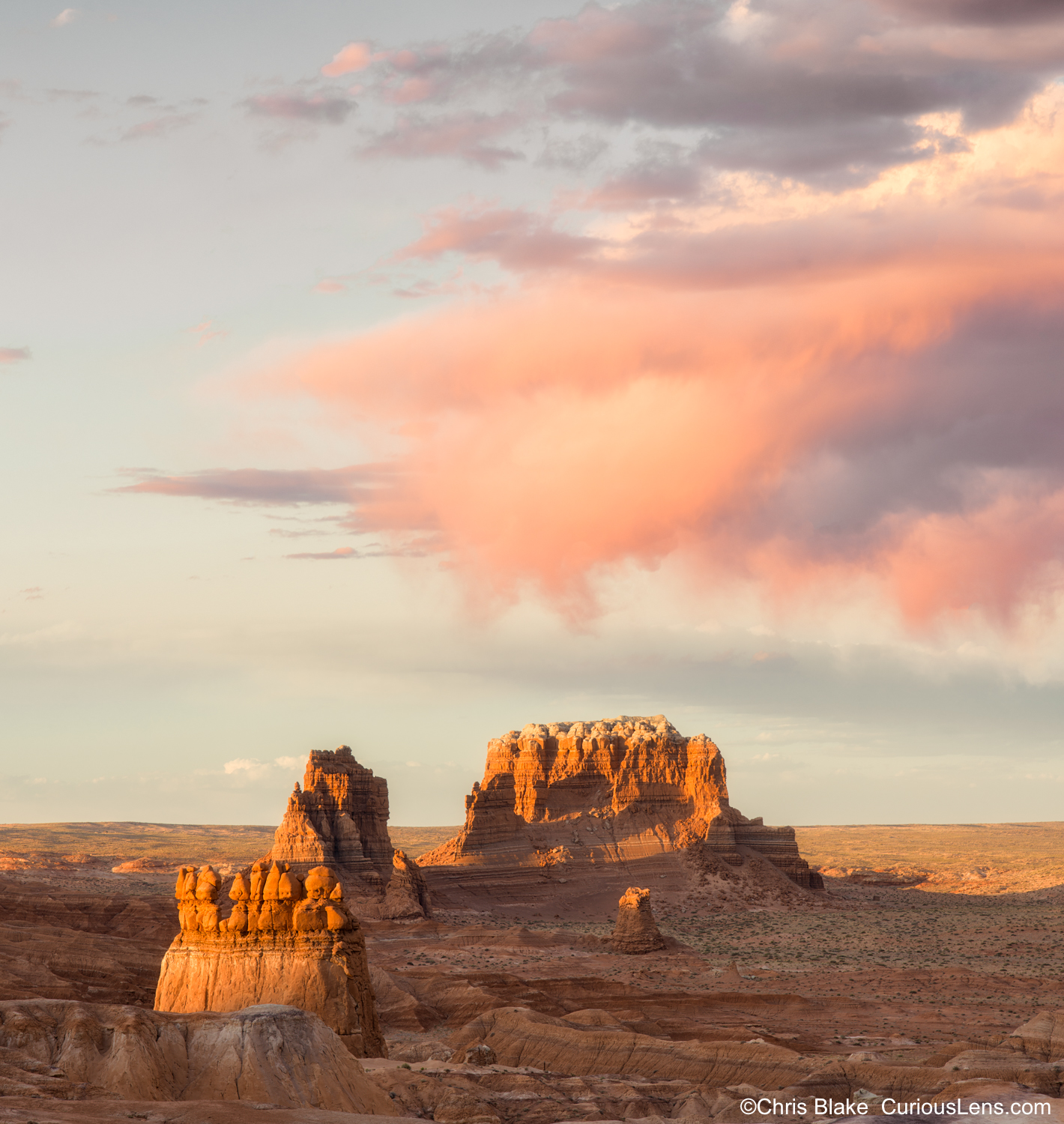 Sunset light on sandstone hoodoos and buttes beneath glowing red clouds in Goblin Valley State Park, Utah.