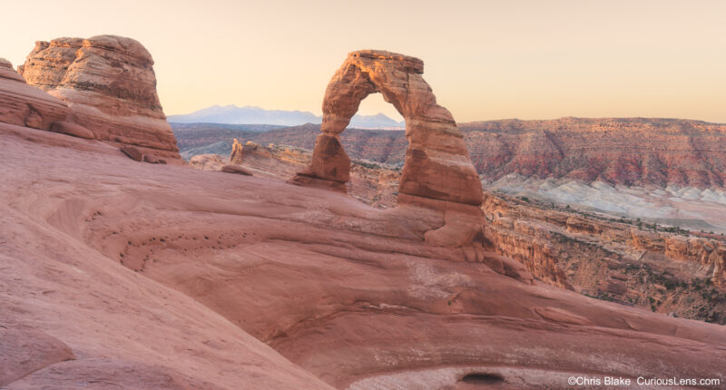 First light on Delicate Arch at sunrise with the La Sal Mountains and desert landscape in Arches National Park, Utah.