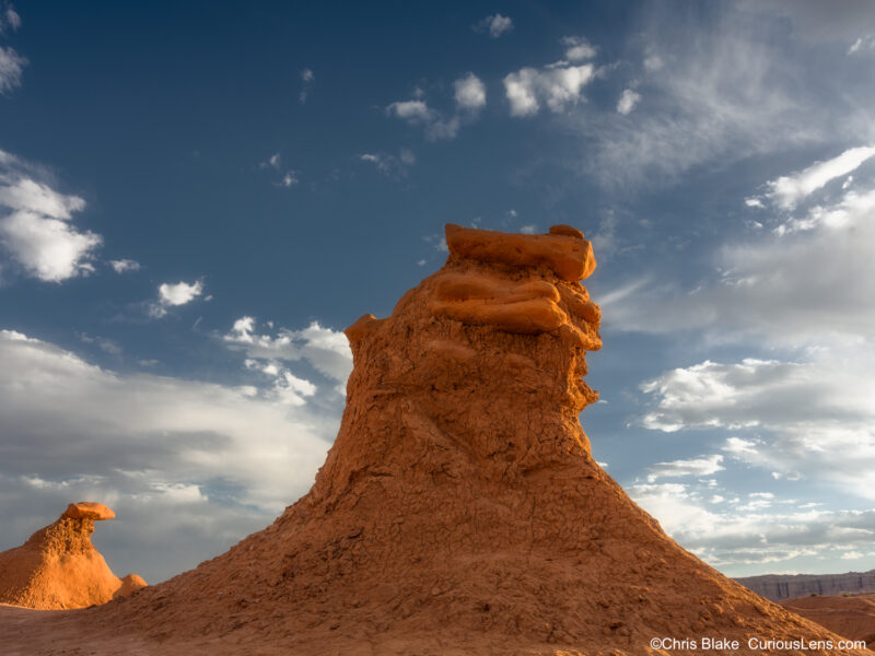Sunset light on a tall sandstone hoodoo beneath dramatic clouds in Goblin Valley State Park, Utah.