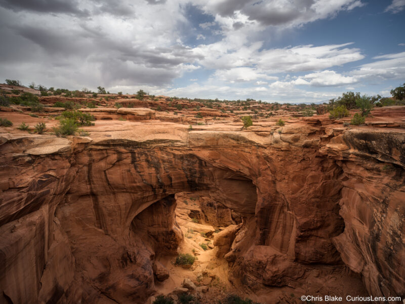 Storm clouds over Gemini Bridges near Moab, Utah, with red sandstone natural bridges and warm light glowing in the canyon below.