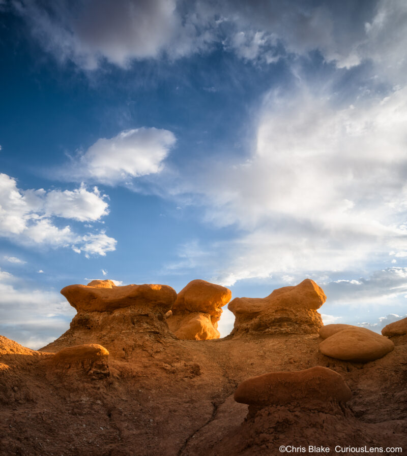 Low-angle view of sandstone goblin formations glowing at sunset beneath a dramatic blue sky in Goblin Valley State Park, Utah.
