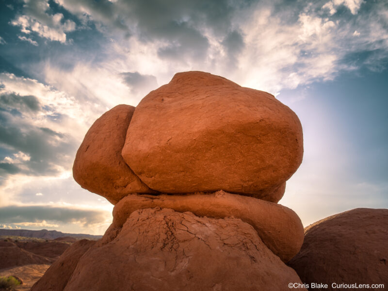 Large rounded sandstone hoodoo formation glowing at sunset beneath dramatic clouds in Goblin Valley State Park, Utah.